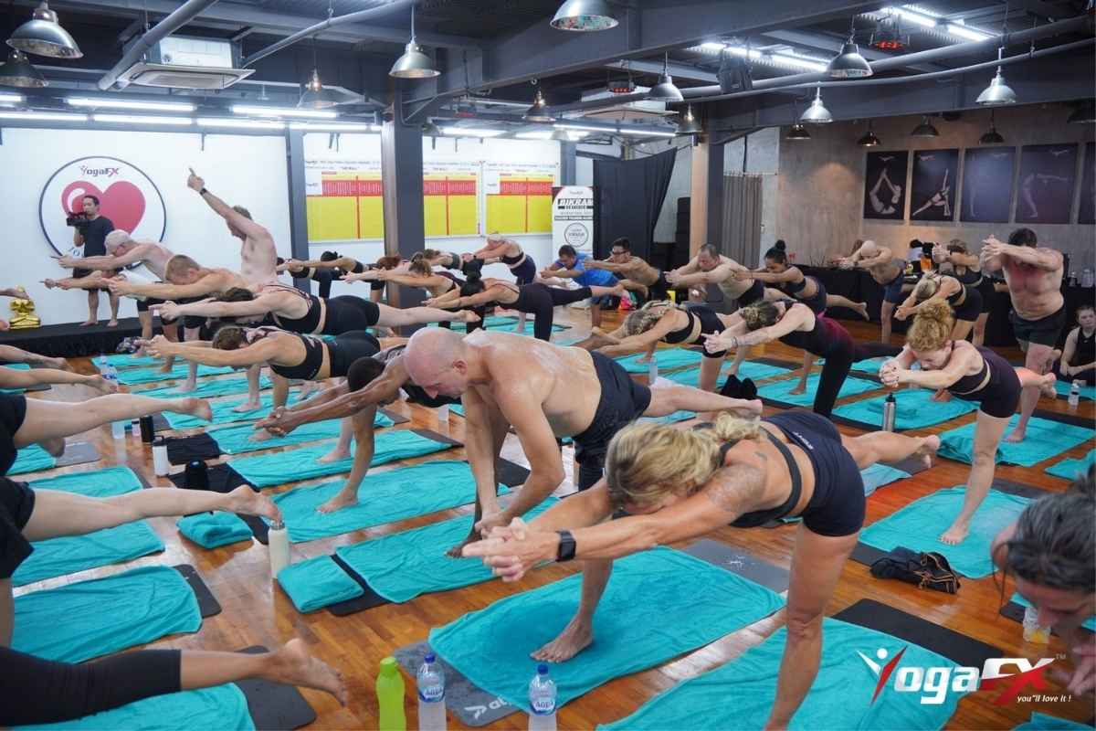 Men and women holding Balancing Stick pose in a heated studio, the kind of class behind questions about hot yoga and male fertility