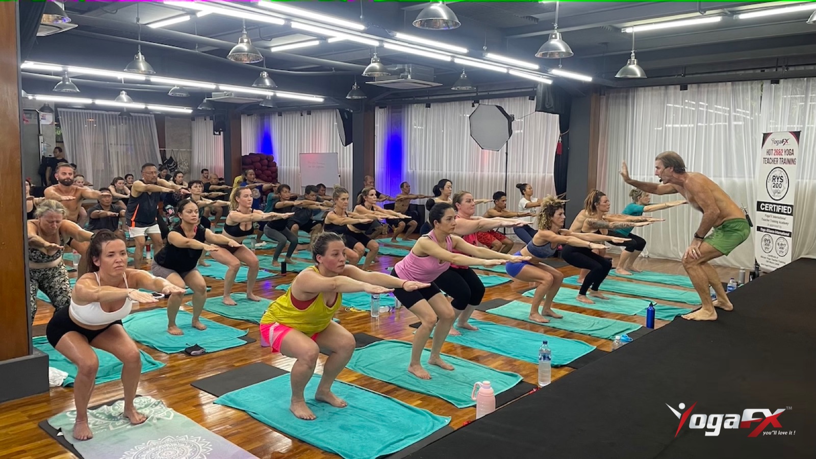 Students hold Chair pose together in a heated studio, a long isometric hold that shows how hot yoga can build muscle